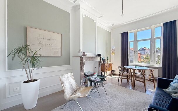 Charmant instapklaar appartement op de 2e verdieping met aangenaam open uitzicht. Inkomhal met vestiairekast. Lichtrijke woonkamer (ca. 22m&sup2;) op authentieke plankenvloer en een schouwelement. Aansluitend de half open keuken voorzien van gasfornuis, dampk