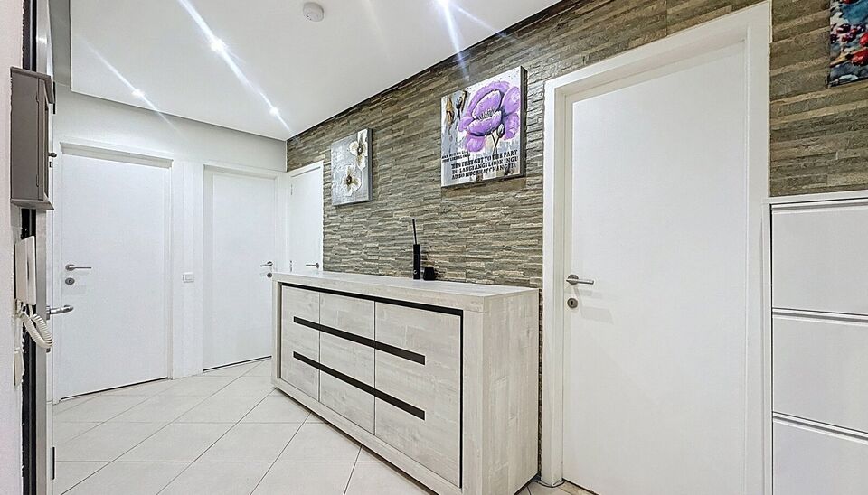 Dit appartement op de tweede verdieping werd recent gerenoveerd. Via de inkomhal bereik je vooraan de lichte woonkamer op tegelvloer. Aansluitend de ingerichte keuken uitgerust met gaskookfornuis, dubbele spoelbak, oven, koelkast met vriesvak en voldoende